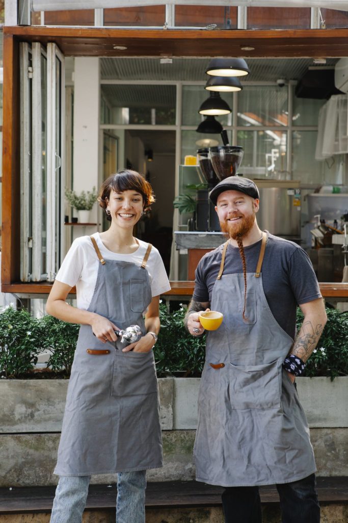 Positive man with cup of coffee and woman with filter holder standing on terrace of modern cafe during work break